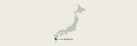 A minimalist map of Japan in muted green-gray on a light warm beige background, with a small labeled pin at the southern tip reading Kirishima.